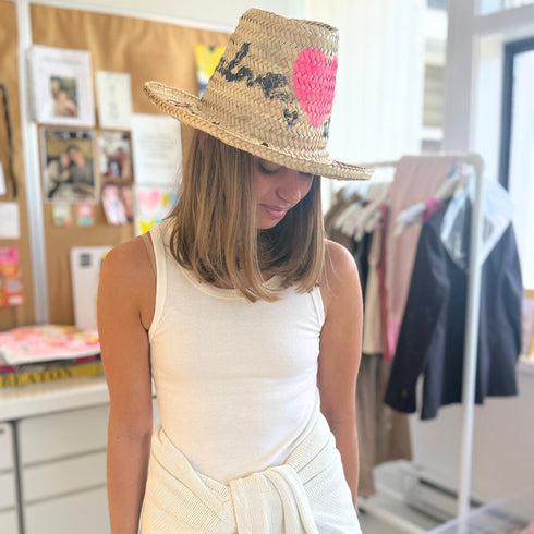 Model wearing a woven straw hat with a hand-painted pink heart and leopard print, paired with a white ribbed tank top by artist Kerri Rosenthal