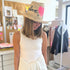 Model wearing a woven straw hat with a hand-painted pink heart and leopard print, paired with a white ribbed tank top by artist Kerri Rosenthal