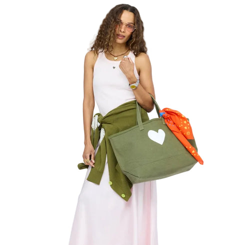 Woman wearing a pink tank and skirt with a jacket tied at the waist, carrying an olive green heart tote bag with an orange heart bandana. Shop womens accessories at Kerri Rosenthal.