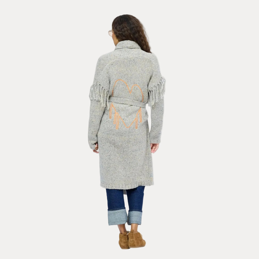 Back view of model wearing a long gray fringe cardigan with an orange open heart embroidered between the shoulder blades.