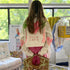 Back view of a model wearing a cream cropped jacket hand-painted with a pink heart, palm trees, and 'Club Love' lettering, with pink heart elbow patches. Handpainted by Kerri Rosenthal