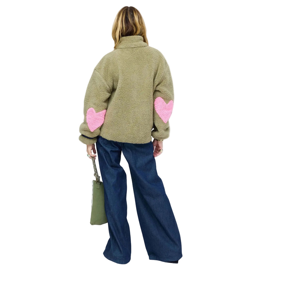 Back of model wearing olive sherpa jacket from behind, showing pink heart-shaped elbow patches and wide-leg denim jeans. Shop Kerri Rosenthal women's jackets.