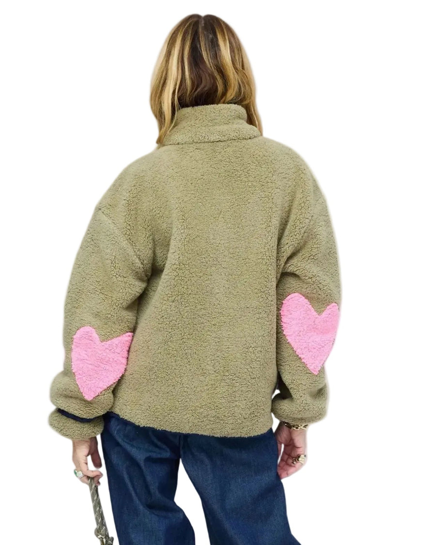 Back of model wearing olive sherpa jacket from behind, showing pink heart-shaped elbow patches and wide-leg denim jeans. Shop Kerri Rosenthal women's jackets.
