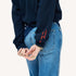Close-up of a woman wearing a Kerri Rosenthal navy cardigan with red 'now and forever' embroidery on the sleeve, styled with blue jeans and a navy heart print bandana.
