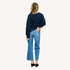 Back view of a woman wearing a Kerri Rosenthal navy cardigan with red sleeve embroidery, styled with cropped blue jeans and black mules.