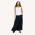 Model wearing a pale pink tank top with a turquoise beaded necklace and a black tiered maxi skirt, paired with woven black flats. Women's clothing by Kerri Rosenthal
