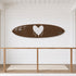 A brown surfboard-shaped decorative plaque or tray featuring a large white dripping heart in the center and a small white script signature on the right side, shown against a plain white background.