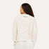 Back view of woman wearing a Kerri Rosenthal cream boucle tweed fringe jacket with white pants.