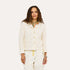 Woman wearing a Kerri Rosenthal cream boucle tweed fringe jacket with gold heart buttons, styled with white drawstring pants and a green beaded necklace.
