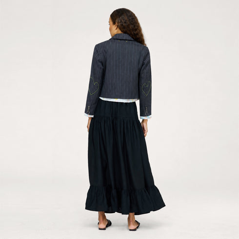 Back view of model wearing a navy pinstriped cropped blazer with heart-embroidered elbow patches over a black tiered maxi skirt