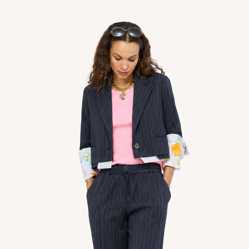 Close-up of Woman wearing a Kerri Rosenthal black pinstripe blazer and matching wide-leg drawstring pants with colorful art-print cuffs, styled with a pink top, gold chain necklace, and sunglasses on her head