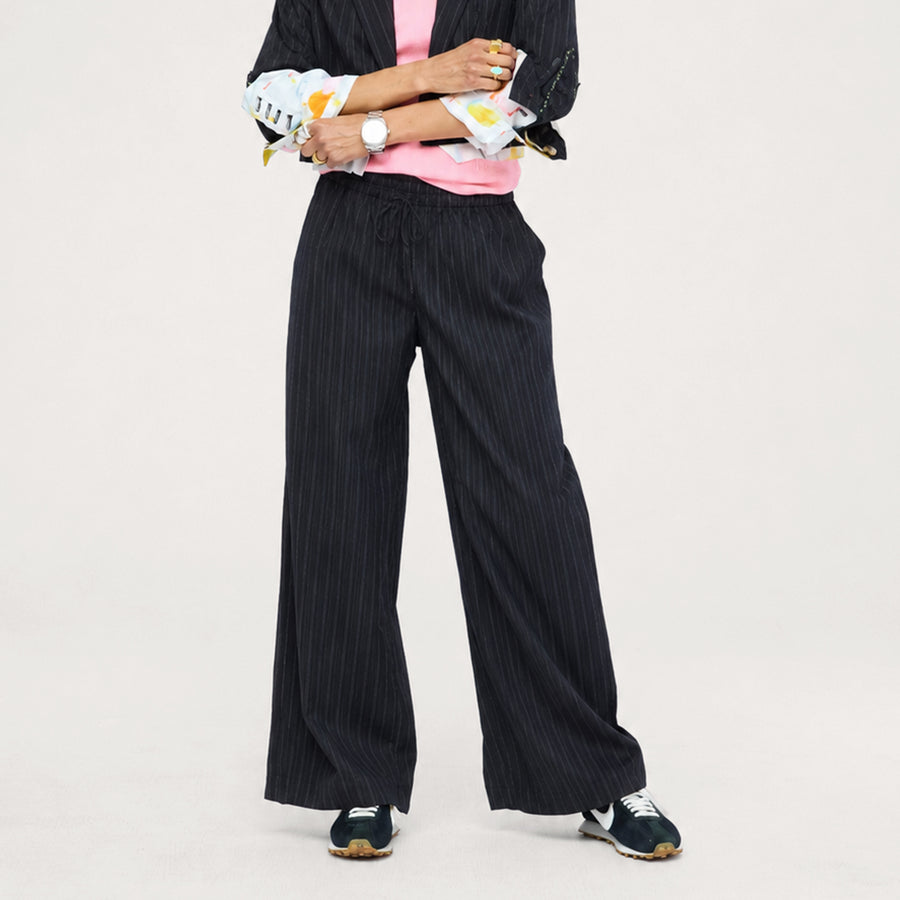 Close-up of black pinstripe pants with a pink top, paint splat-cuffed jacket, and sneakers