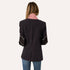 Back view of a woman wearing a coal blazer with heart embroidery on the sleeves, a pink collar, and jeans.