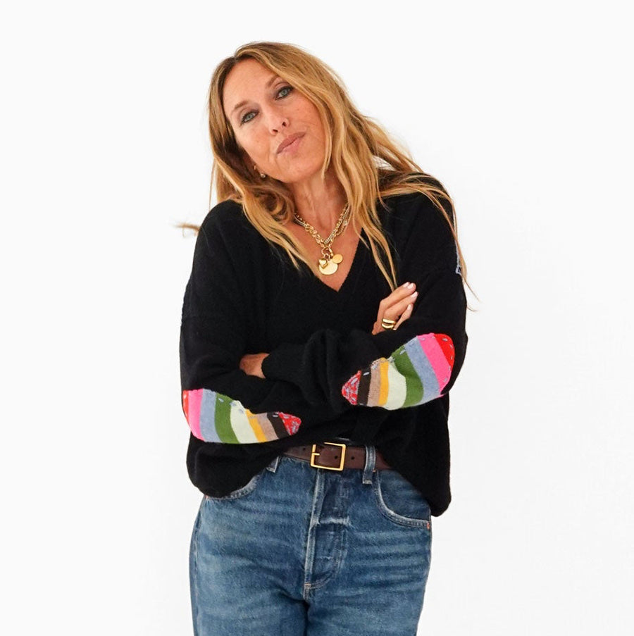 Kerri wearing the Frenchie Patchwork Sweater in black with multicolor striped elbow patches and jeans, arms crossed, front view