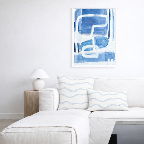 Large rectangular abstract Kerri Rosenthal artwork featuring blue, gray, and black hearts and stars with vertical paint drips, hanging on a neutral wall above a modern white sectional sofa styled with matching blue patterned pillows.
