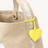 Close-up of a tan canvas tote bag showing the branded strap detail and yellow heart keychain charm.