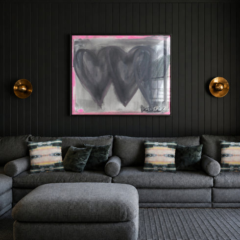 Holding Hearts art print by Kerri Rosenthal with three black hearts and grey ground and pink outline in a black frame displayed on a living room wall with black couch with Kerri Rosenthal Lemonade pillows and black wall treatment.