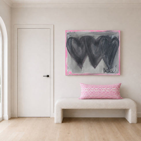 Close-up of hand-painted 3 black connecting hearts and gray and pink background texture and brushstrokes on Holding Hearts art print on canvas in room with Kerri Rosenthal pink palm ikat print lumbar pillow.