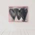 Abstract painting with three black hearts on a pink background, signed 'Kerri', in a minimalistic setting.