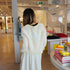 Kerri standing in the Westport flagship shop wearing a white open-knit crochet cardigan with large neon yellow-green trim and heart on the back and white flowy maxi dress.