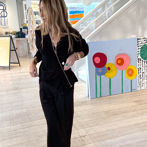 Woman in a black outfit standing next to a colorful floral painting in an indoor setting.