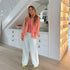 Kerri standing in a retail store wearing a coral pink oversized linen shirt, coral ribbed tank top, light denim palazzo wide leg white trousers, and lime green mule sandals.