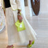 Kerri wearing a cream crochet Frankie cardigan with neon yellow-green trim, a white flowy maxi kr two tone tank dress and lime green wedge sandals, holding a chartreuse heart clutch bag indoors.
