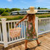 Kerri walking on a sun-lit boardwalk wearing her pink toile sarong wrap skirt, pink KR tank, and wide brim straw hat, carrying a matching pink toile canvas tote bag.
