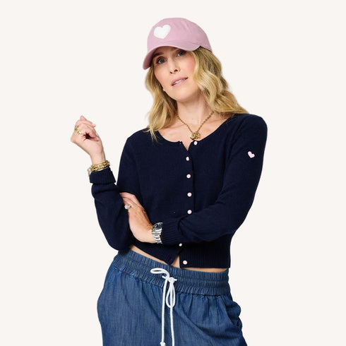Charmed indigo blue button-down cashmere cardigan with an embroidered tiny heart and pink baseball cap hat by Kerri Rosenthal