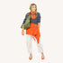 Woman wearing a navy striped top with an orange sweater tied at the waist, an orange bandana, cream pants, orange heels, and an olive bag.