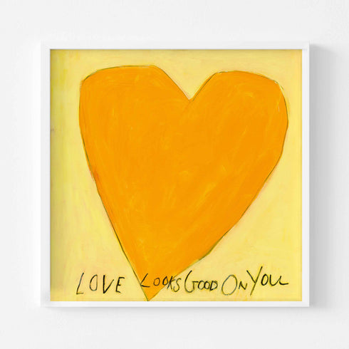 Love Looks Good on You art print: a bold orange heart with an angular shape on a pale yellow background, with "Love Looks Good On You" hand-painted below it in black, in a white frame