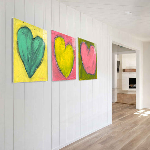 Love Note 2 art print: a tall green-teal heart with thick textured brushstrokes on a bright yellow background, signed in pink, hung in a room setting, shown at a three-quarter angle