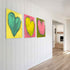 Love Note 2 art print: a tall green-teal heart with thick textured brushstrokes on a bright yellow background, signed in pink, hung in a room setting, shown at a three-quarter angle