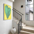 Love Note 2 art print: a tall green-teal heart with thick textured brushstrokes on a bright yellow background, signed in pink, hung in a room setting