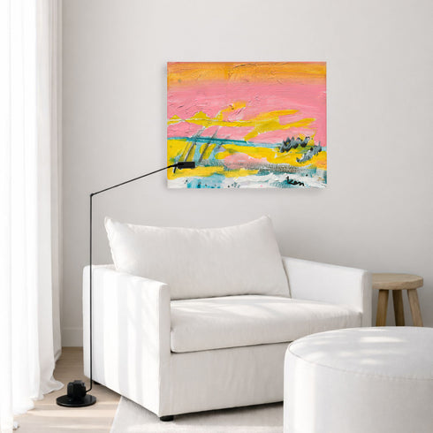 Sunset Summer art print: a pink and yellow sunset landscape hung on a pale gray wall above a white armchair, a black arc floor lamp and a wooden stool in a bright living room