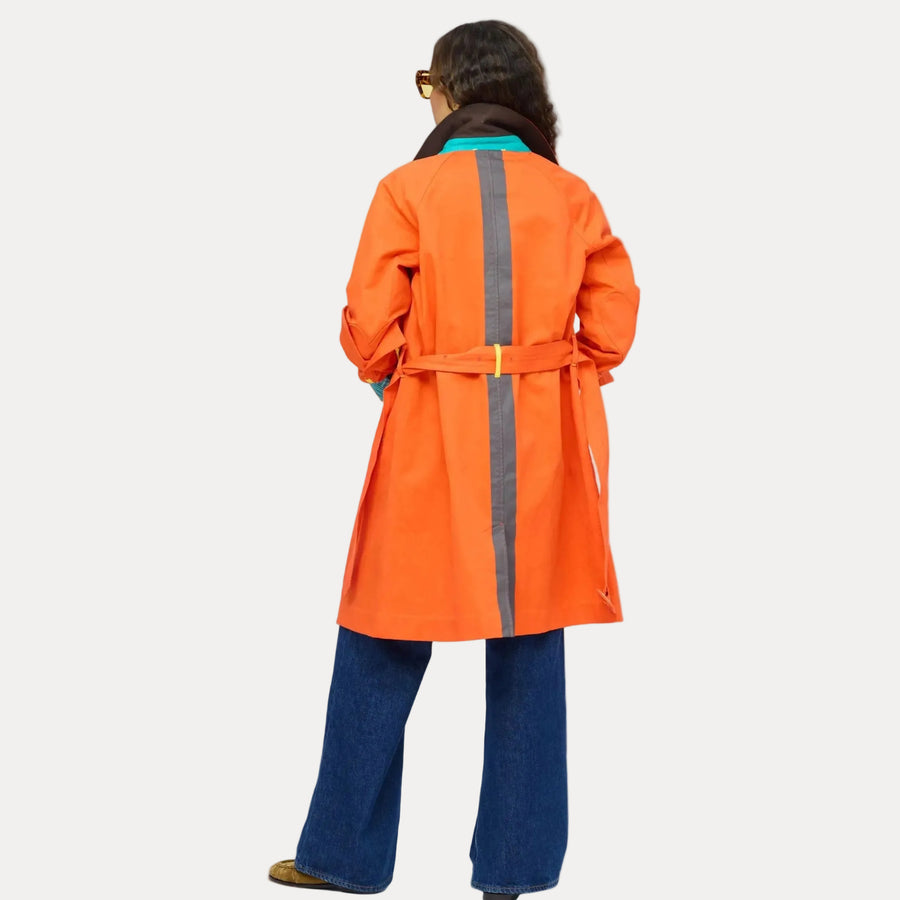 Back of woman wearing the KR Trench Coat in orange, a double-breasted colorful trench with teal contrast undercollar, styled with wide-leg denim jeans. Shop Kerri Rosenthal outerwear.