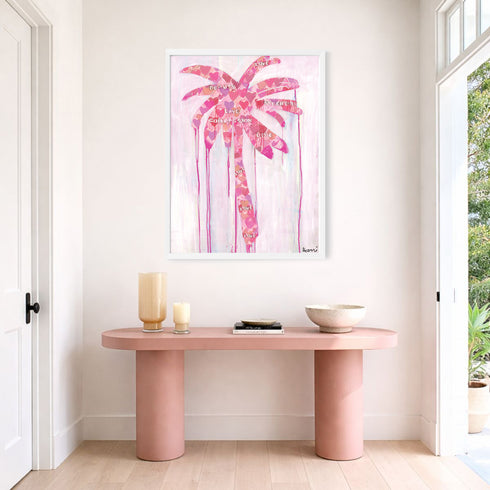 Where Love Grows art print: a pink heart-patterned palm tree on a pale pink ground, in a white frame, hung above a blush-pink console table in a bright entryway
