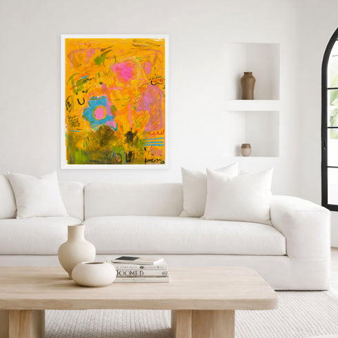 Wild Love Garden art print: a golden-orange painting with a blue flower, pink blossom and black handwritten marks, in a white frame, hung above a white sofa in a bright living room