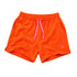 Bright orange athletic shorts with a pink drawstring and a small pink heart logo on the lower left leg, displayed on a light beige background.