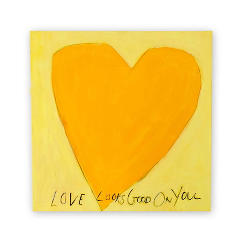 Oversized amber heart on soft butter-yellow canvas with the handwritten phrase LOVE LOOKS GOOD ON YOU in charcoal script below