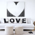 White sofa with 'LOVE' cushions, two ottomans, and a heart-shaped abstract painting in a living room.