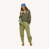 Woman wearing a green v-neck sweater with a blue drippy heart bandana, army green drawstring pants, and tan suede loafers.