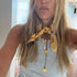 Woman with long blonde hair wearing a gold necklace accessory indoors.