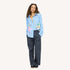 Woman wearing an open blue striped shirt with colorful art print by artist Kerri Rosenthal, navy pinstripe pants, and sneakers.
