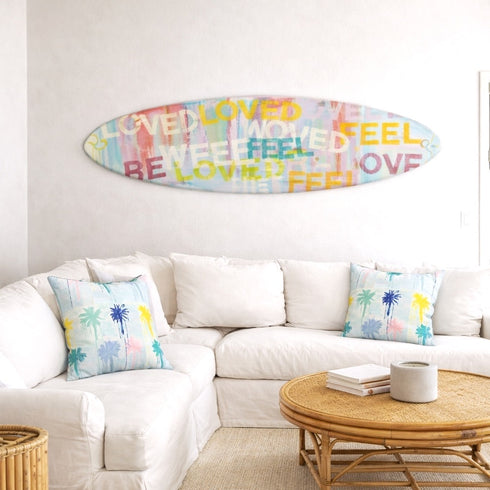 Decorative surfboard with colorful text above a white sofa in a living room.