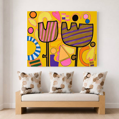 A colorful abstract canvas print featuring stylized tulips and geometric shapes in yellow, pink, purple, orange, and black, displayed on a white wall above a light wood bench with three patterned throw pillows.