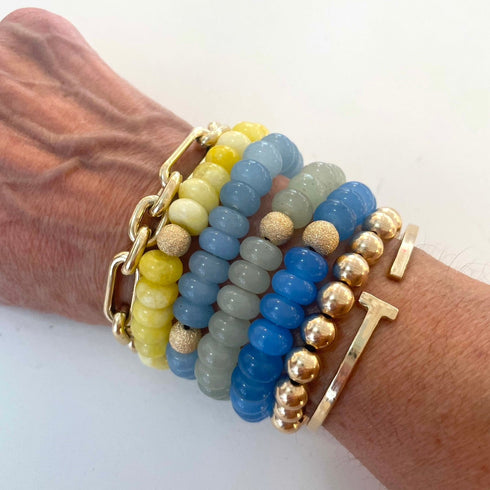 Wrist wearing multiple beaded bracelets with gold accents on a white background