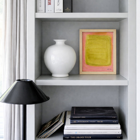 Bookshelf with a white vase, framed abstract art, and books.