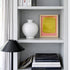 Bookshelf with a white vase, framed abstract art, and books.