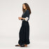 Side view of a woman wearing a Kerri Rosenthal black tiered maxi skirt styled with a black pinstripe blazer, a white art-print shirt, and black woven flat sandals.